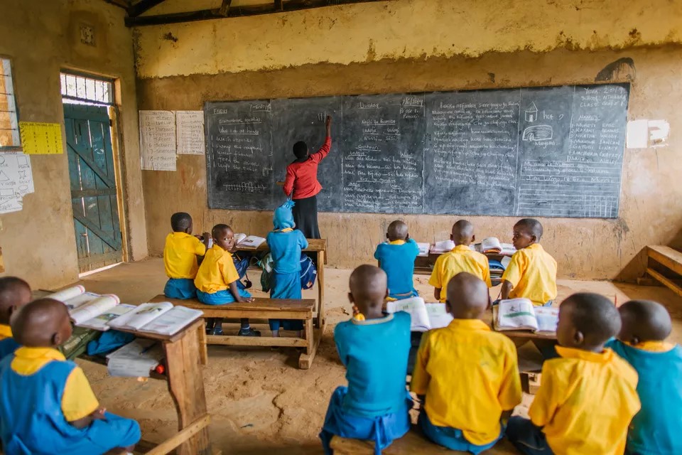 Students watch attentively as teacher writes on chalkboard