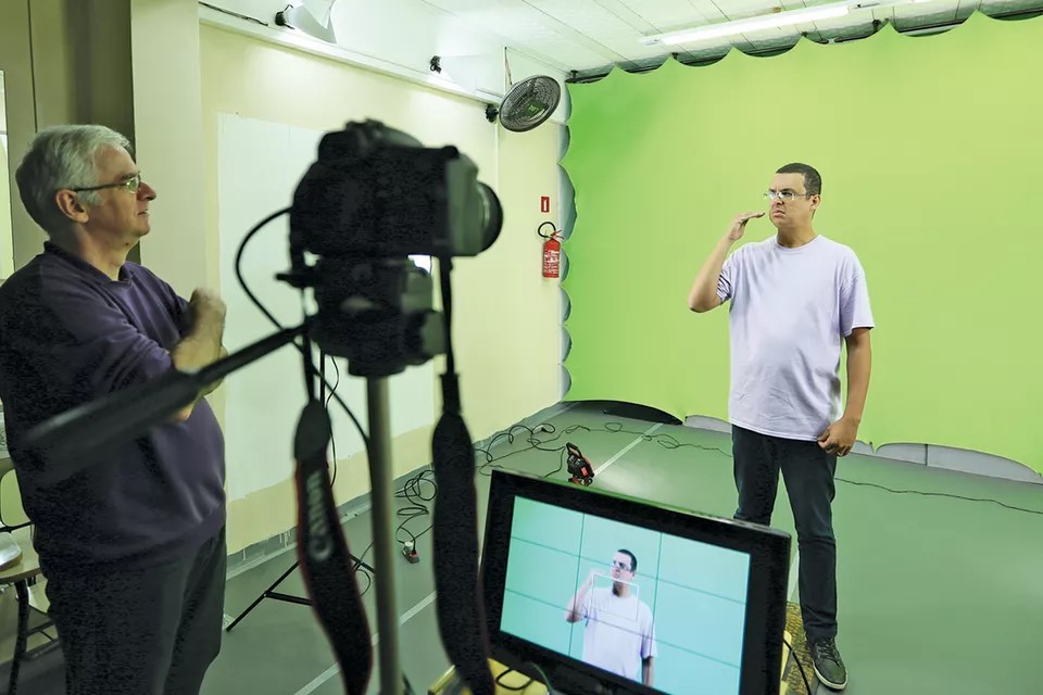 Carlos signs in Brazilian Sign Language in front of a green screen