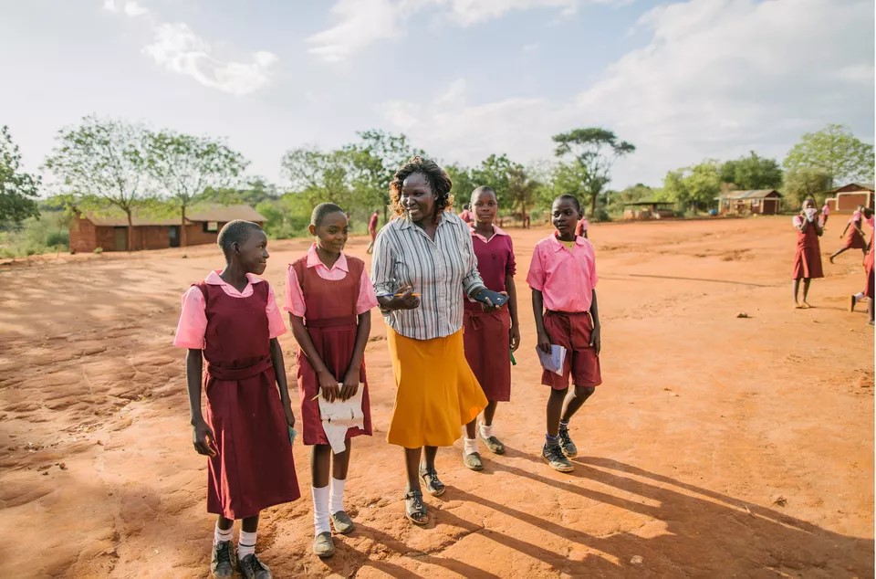 Teacher and students walking along red dirt in Kenya