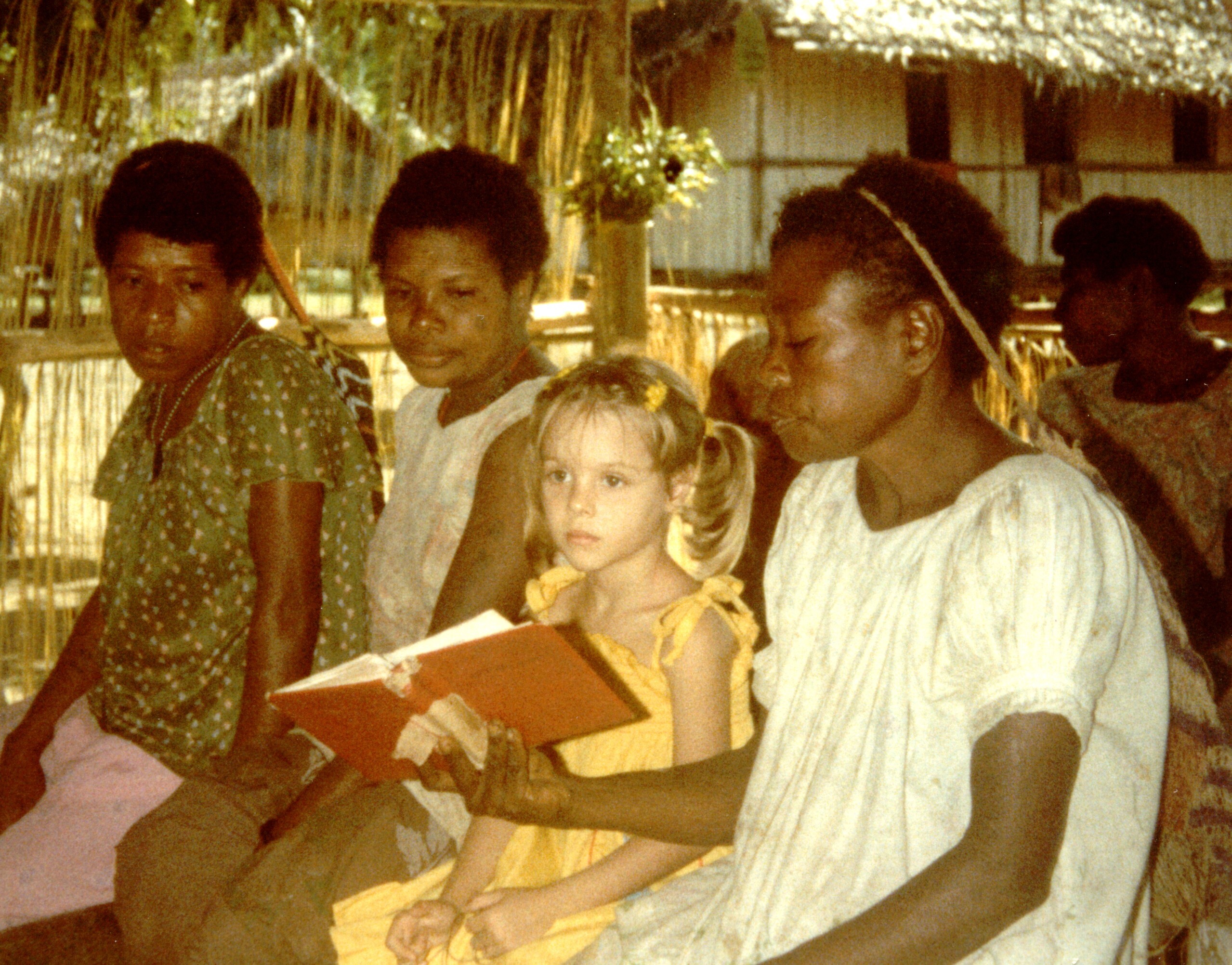 A little American girl sits in a church surrounded by local believers in Papua New Guinea