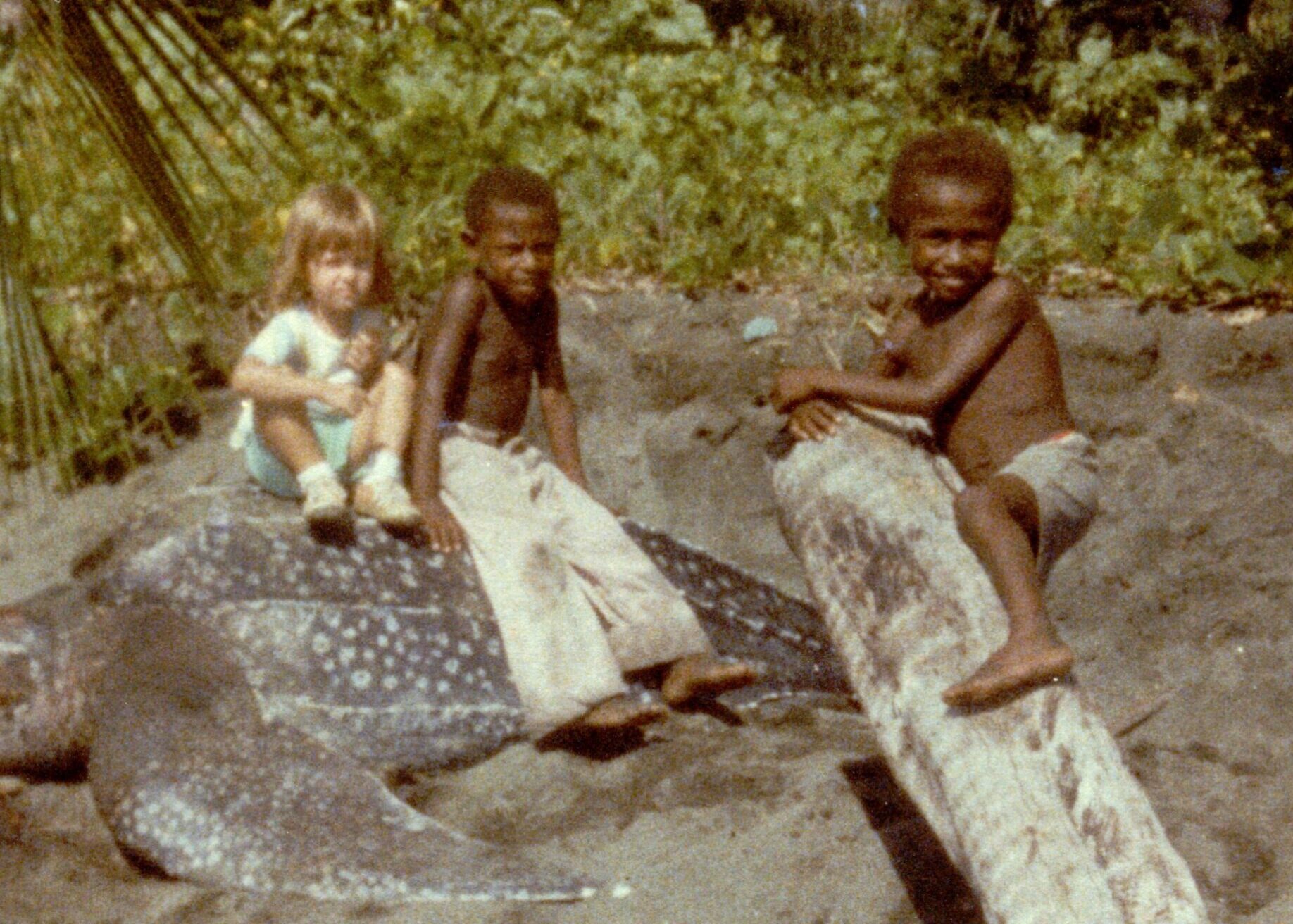 Little American girl sits on tortoise with friends in Papua New Guinea