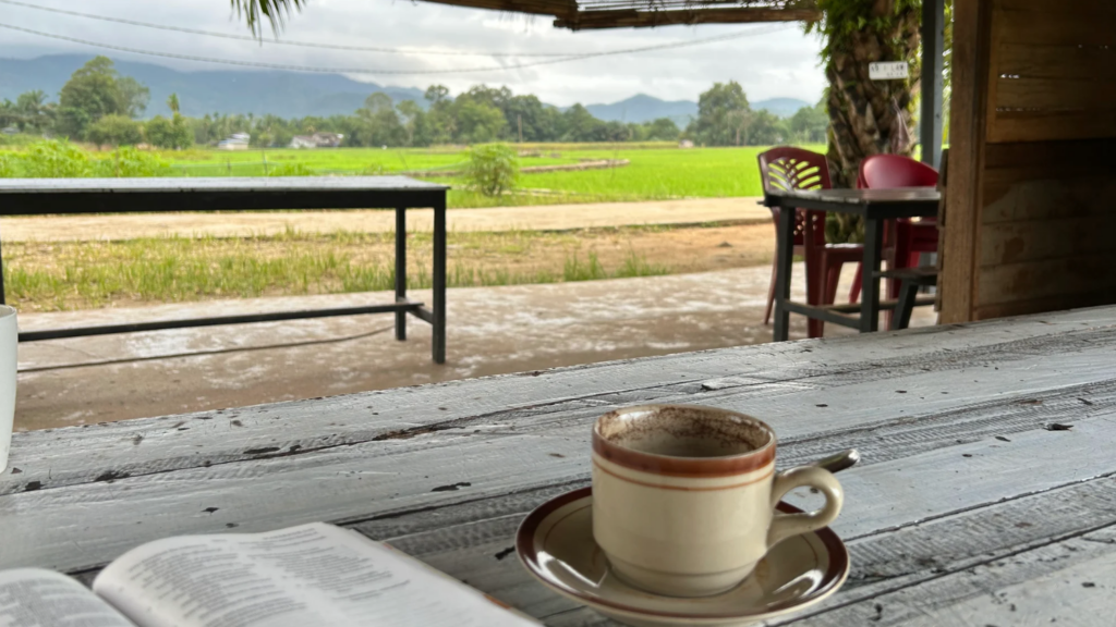 An open Bible sitting next to a cup of coffee on the table